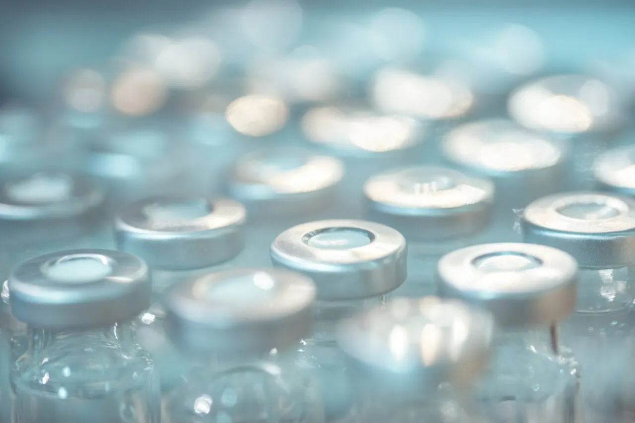 A researcher in a laboratory holds a vial of an experimental mRNA cancer vaccine beside lab equipment.