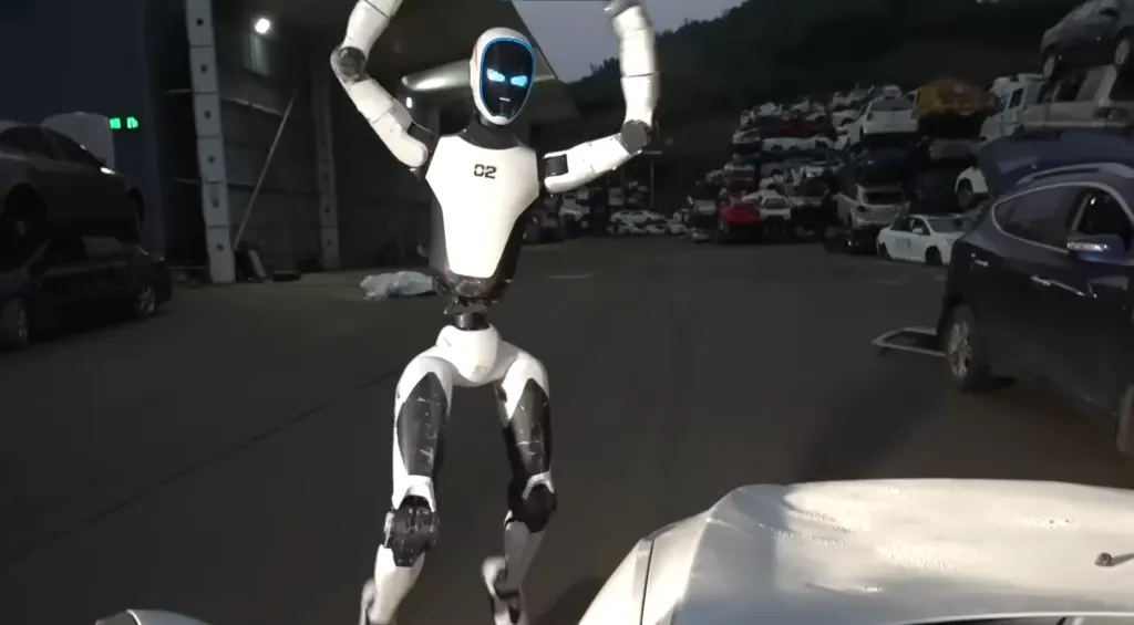 A Unitree humanoid robot standing in a lab as engineers monitor its training on screens.