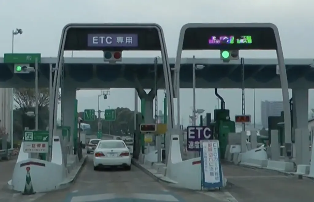 Cars queuing at a Japanese highway toll gate with the barrier raised during an electronic toll system outage.