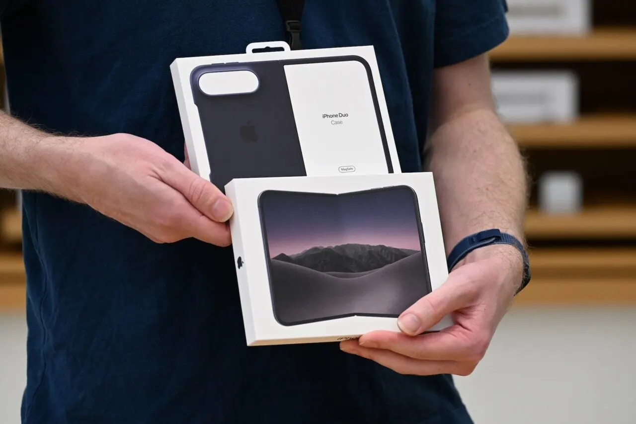 An Apple Store employee handing a sealed iPhone box back across the counter to a customer.