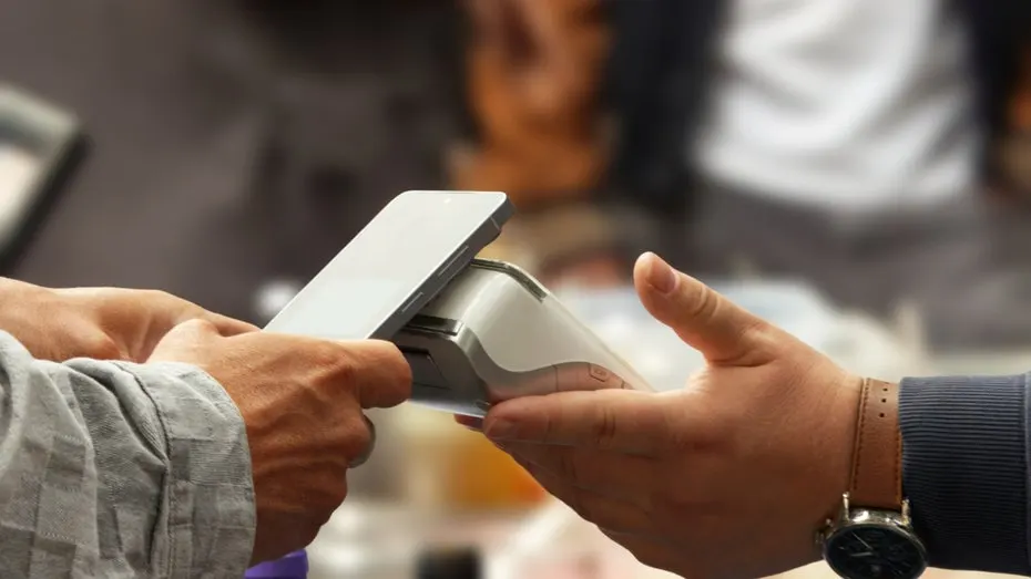 A sales advisor in an electronics store holds a mobile card terminal while a customer pays by card.