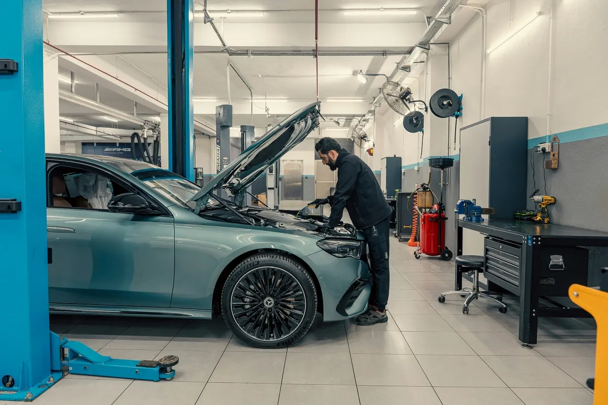 A car undergoing an inspection at a vehicle testing center, with a warning icon over a smartphone showing a fake fine text message.