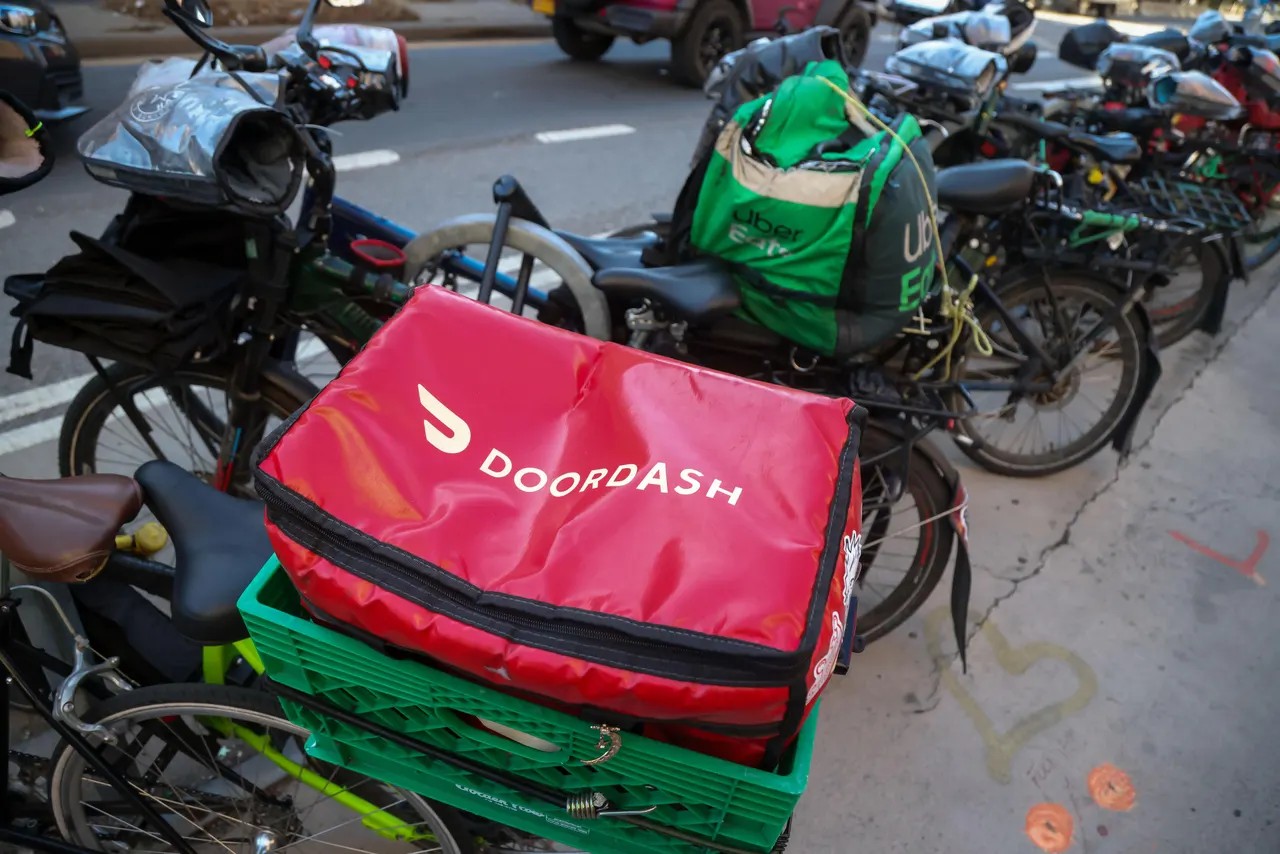 A DoorDash delivery courier carrying grocery bags to a customer's front door.