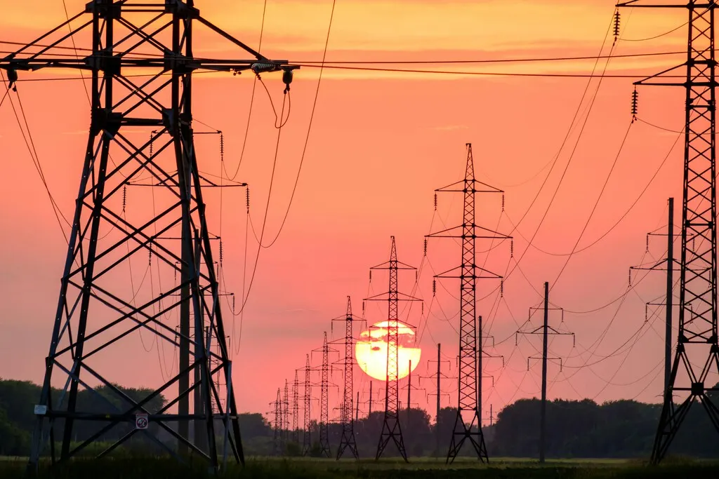 Combined-cycle power plant with cooling towers and high-voltage lines at dusk in Spain.