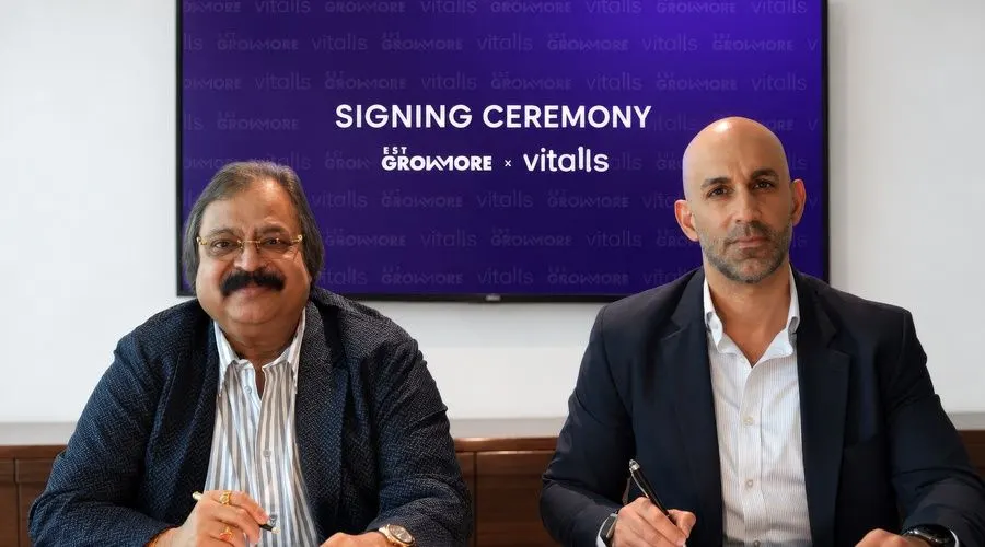 Founder and investor signing an agreement on stage at a health summit, with a smartphone showing a digital health passport app.