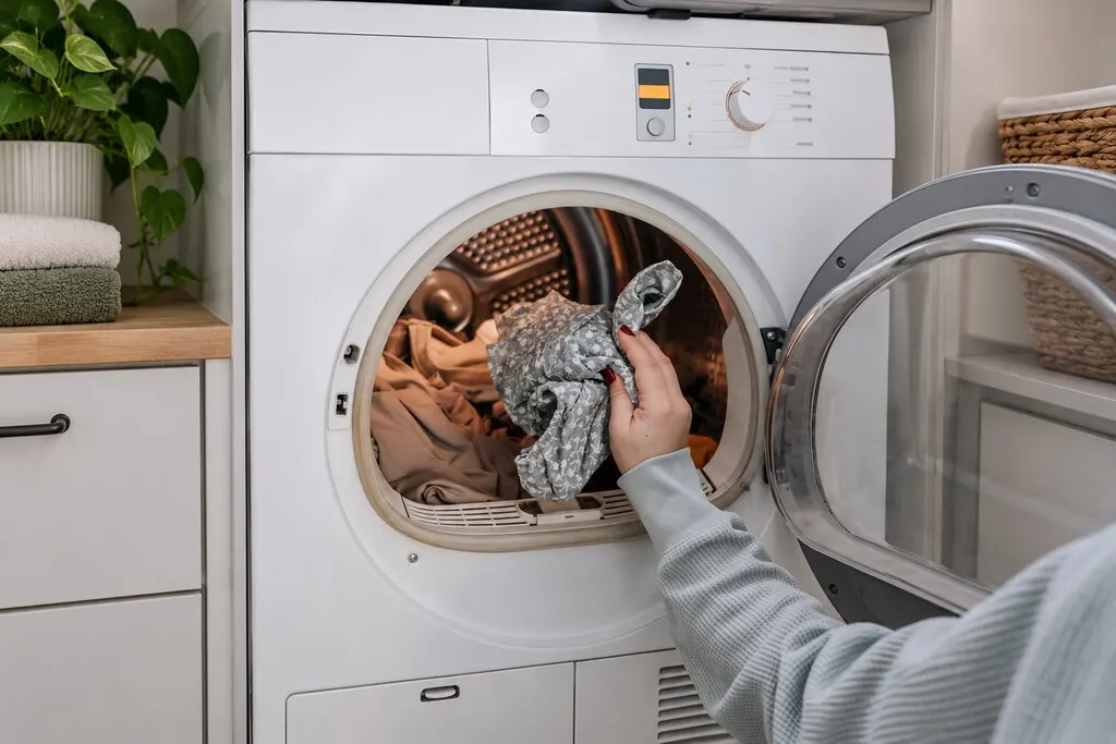 Washing machine in a Spanish home with rooftop solar panels visible through the window in bright sunlight.