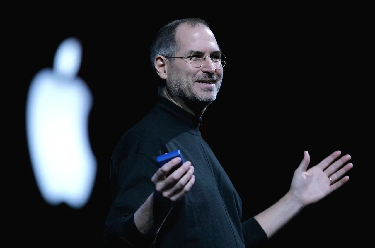 A MacBook Pro with an OLED touchscreen display being touched by a user's finger on a desk.