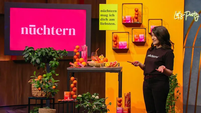 A founder presents small sachets for alcohol-free spritz drinks to a panel of investors in a TV studio.