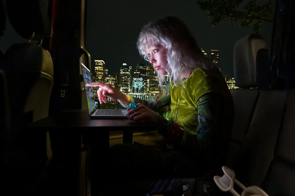 A MacBook Pro with an OLED touchscreen display open on a desk showing a bright colorful interface.