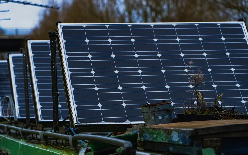 Rows of solar panels at a large solar farm under a blue sky with a control cabinet in the foreground.