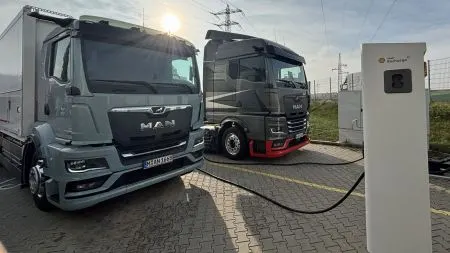 An electric MAN eTGX semi-truck connected to a bidirectional DC charging station at a freight depot in Regensburg.